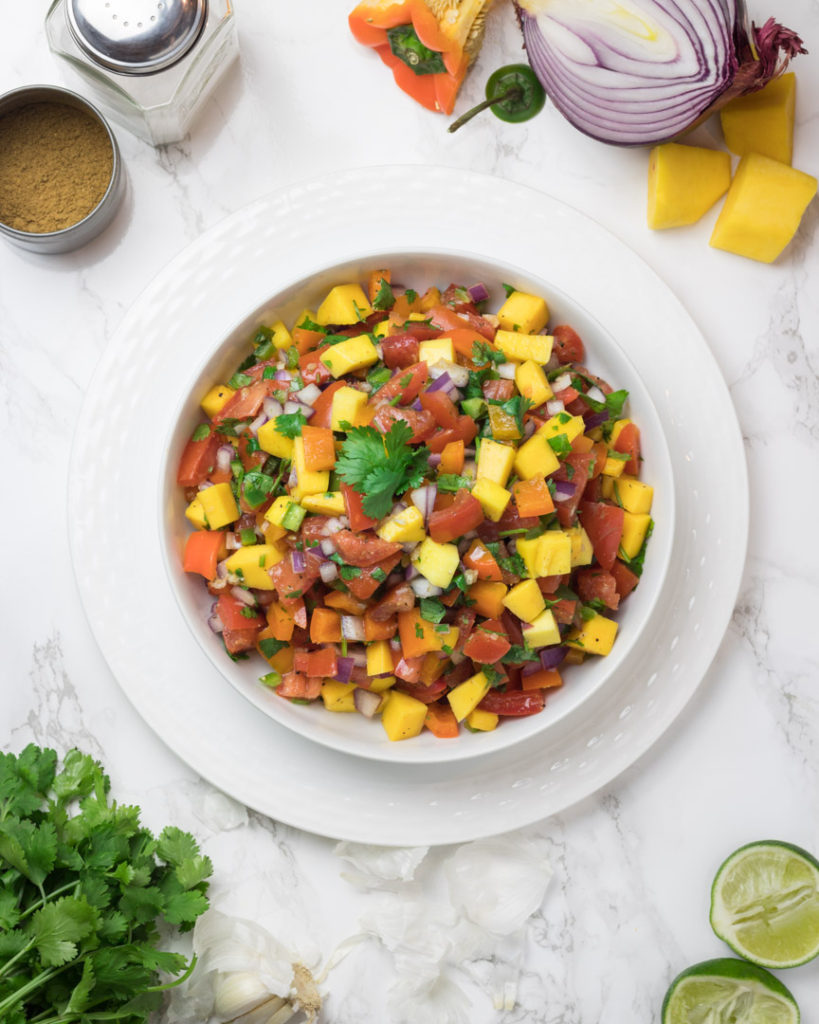 Colorful mango salsa surrounded by the ingredients 