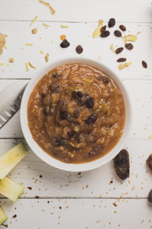 Sweet and spice apple chutney in a bowl surrounded by it's ingredients.