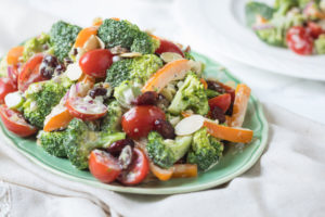 Creamy broccoli salad with tomatoes and dried cranberries on a green plate