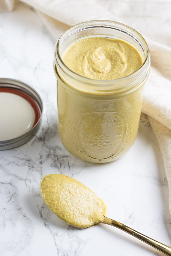 Creamy cashew alfredo sauce in a jar with a spoonful on the table