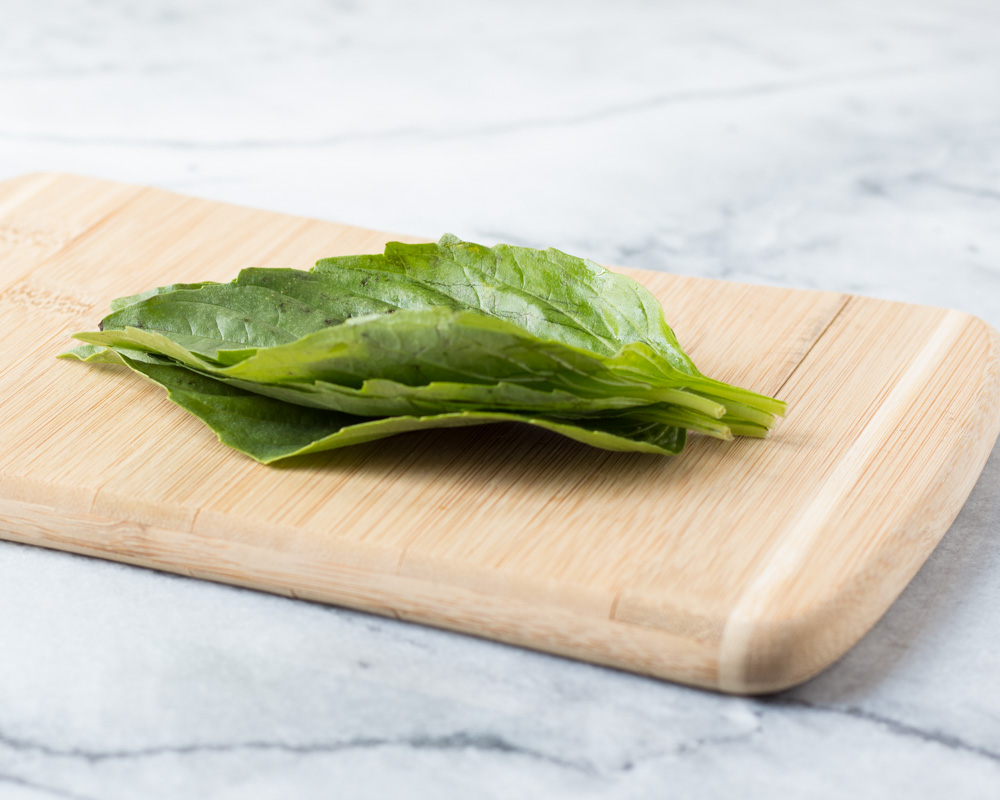 Basil leaves stacked on top of each other on a cutting board.