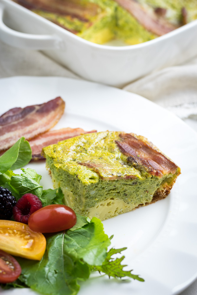 A slice of pesto fritatta with bacon, a salad and a side of bacon...served on a white plate.
