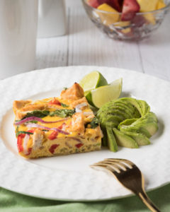 Slice of Thai red curry chicken fritatta with avocado and lime wedges.