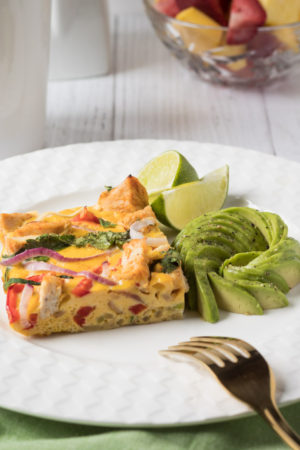 Slice of Thai red curry chicken fritatta with avocado and lime wedges.