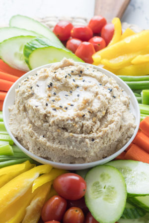 Close-up of cauliflower hummus in a bowl surrounded by colorful veggies