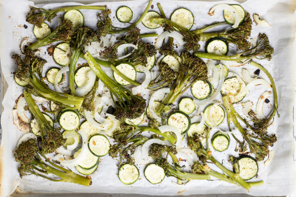 Raw and roasted zucchini, broccolini and onions on sheet pans.