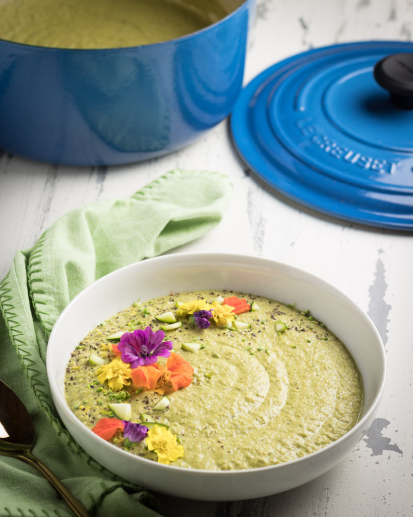 Creamy Zucchini and Broccolini Soup decorated with edible flowers along with a pot in the back. 