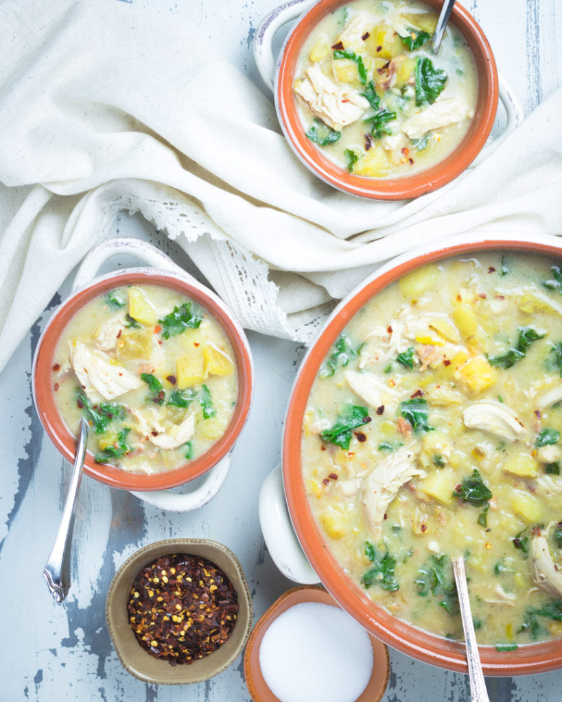 Large and small crocks of chicken and kale chowder soup on a table
