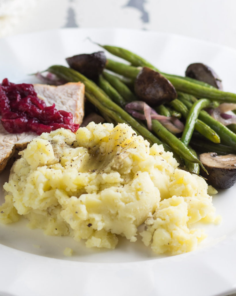 Golden mashed potatoes with turkey topped with cranberry sauce and a side of green beans with mushrooms. 
