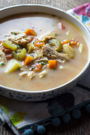 Crock pot chicken and herb soup in a while bowl on a colorful linen napkin
