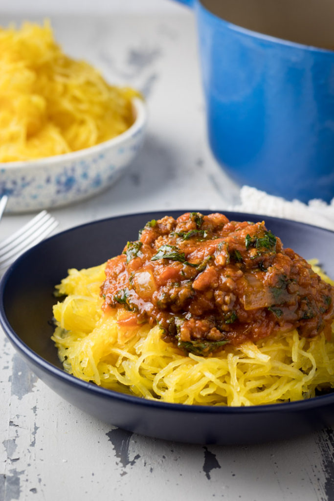 Red sauce with meat and veggies piled on roasted spaghetti squash on a blue plate
